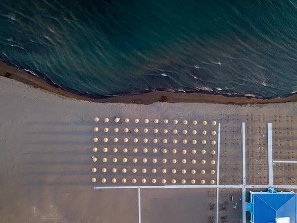 Вид с воздуха на песчаный пляж с желтыми шезлонгами и деревянными зонтиками на закате — стоковое фото