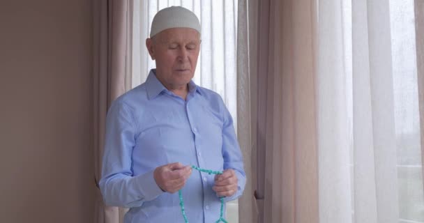 Een oude man met rozenkransen biddend — Stockvideo