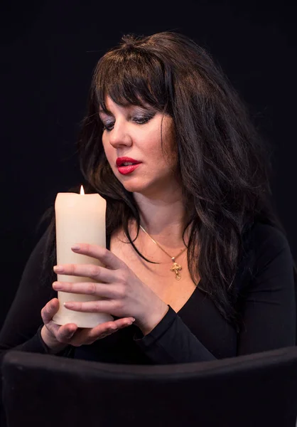 Mystic young women with candle on black background