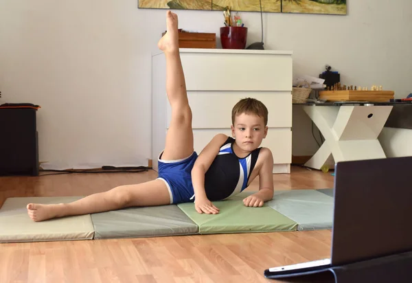 Little gymnast boy is training online with laptop at home