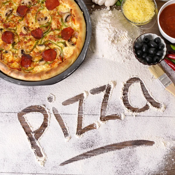 A palavra Pizza escrito em farinha com vários ingredientes . — Fotografia de Stock