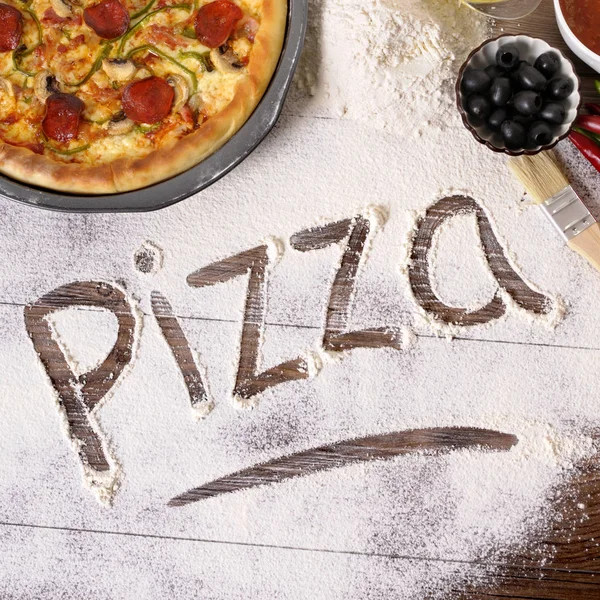 La palabra Pizza escrita en harina con varios ingredientes . — Foto de Stock