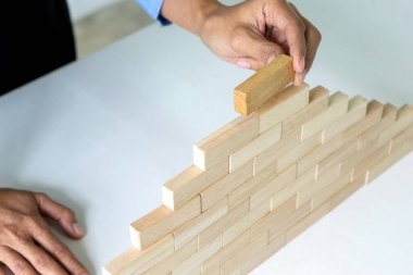 Genç işadamı ahşap tuğla bloktan duvar ve kule inşa etmeye çalışıyor.