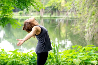 50 yaşından büyük bir kadın park alanındaki göl kenarında yoga yapıyor. Doğada güzel bir günün ve pozitif enerjinin tadını çıkar. 