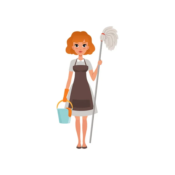 Linda mujer pelirroja de pie y sosteniendo fregona y cubo. Servicio de limpieza. Dama de casa vestida con vestido, delantal y guante protector. Diseño de vector plano — Vector de stock