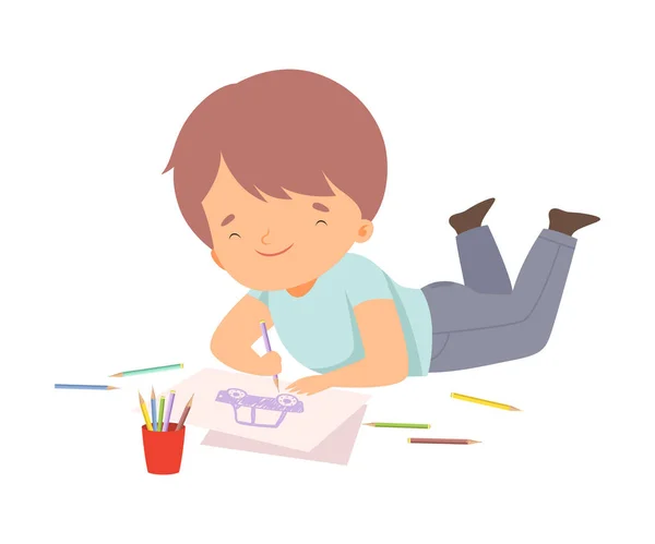 Leuke jongen Liggend op zijn buik en tekening afbeelding met kleurrijke potloden, Schattige jonge kunstenaar stripfiguur, Kids creatieve Hobby Vector Illustratie — Stockvector