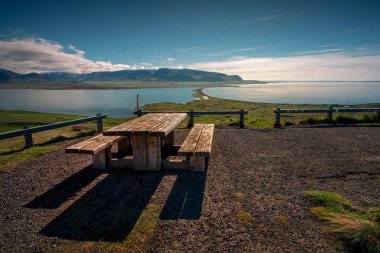 Okyanus kıyısındaki ahşap banktan dağ manzarasına