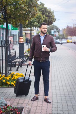 Turizm için bavulu olan yakışıklı bir adam. Seyahat için evden çıkın. Modaya uygun giyinen adam ve kahve. Stok Fotoğrafı.