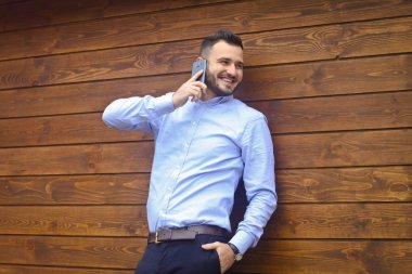 Ahşap bir arka planda gömlekli yakışıklı bir adamın portresi. İş adamı, şık giyinmiş patron. Telefonda konuşan seksi bir adam. Stok Fotoğraf Tasarımı