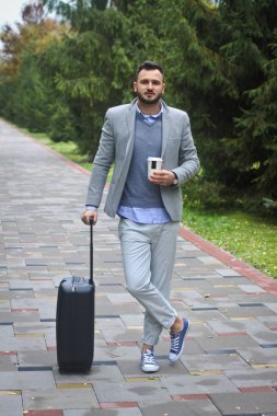 Modaya uygun giyinmiş adam arka planda bir yol ve ağaçlarla seyahat ediyor. Adam aceleyle uçup kahve ve çay dolduruyor. Tasarım için stok fotoğrafı