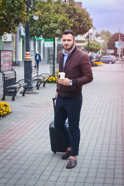 Schöner Mann mit einem Koffer für den Tourismus. Verlassen Sie das Haus für Reisen. modisch gekleideter Typ und Kaffee. Archivbild. — Stockfoto