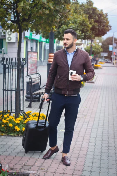 Schöner Mann mit einem Koffer für den Tourismus. Verlassen Sie das Haus für Reisen. modisch gekleideter Typ und Kaffee. Archivbild. — Stockfoto