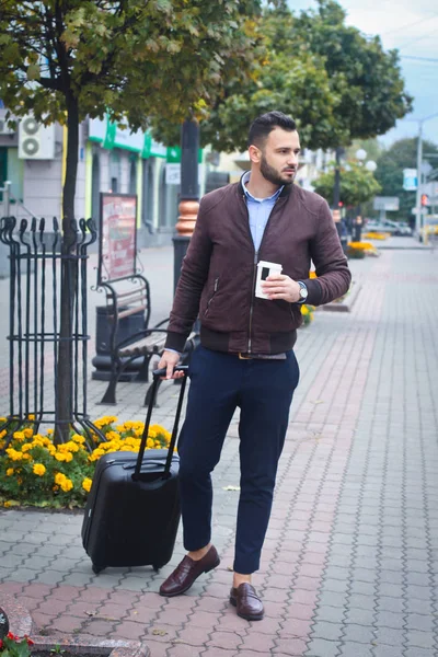 Красивый мужчина с чемоданом для туризма. Выходите из дома для путешествий. Модно одетый парень и кофе. Фондовое фото . — стоковое фото
