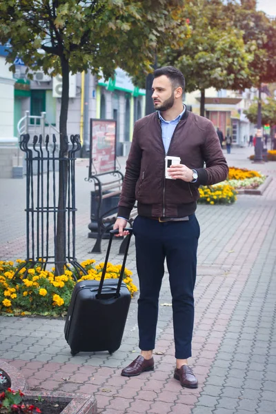 Schöner Mann mit einem Koffer für den Tourismus. Verlassen Sie das Haus für Reisen. modisch gekleideter Typ und Kaffee. Archivbild. — Stockfoto