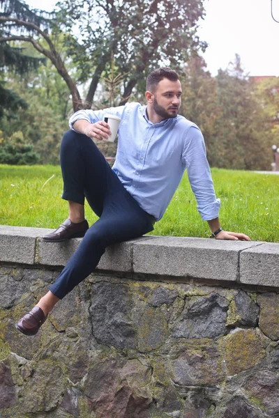셔츠를 입은 남자가 유럽 도시 공원에 앉아 있는 사진. 나무와 건물의 배경에 있는 남자. Stock photos — 스톡 사진