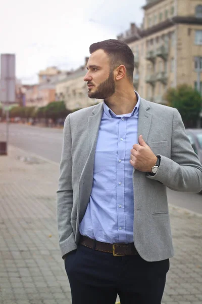 Retrato de un hombre de negocios en la calle cerca de la carretera de una ciudad europea. Un hombre guapo barbudo vestido con estilo. Un hipster de moda. Fotos de stock —  Fotos de Stock