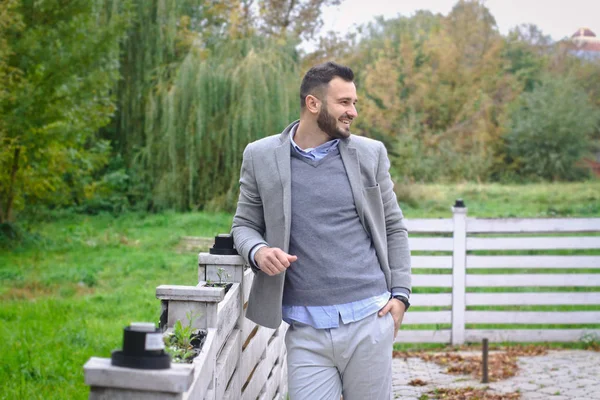 Portrait of a sexy man dressed in a suit. Fashionable guy in the autumn nature near a white wooden fence. Businessman relaxes. Skok photo for design — Stock Photo, Image
