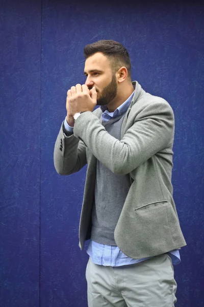 Un hombre vestido a la moda contra una pared azul. Invierno frío, clima de otoño. Un tipo que se calienta. Foto de stock para el diseño —  Fotos de Stock