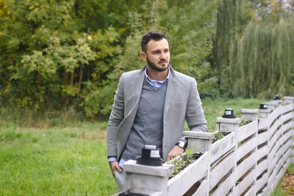 Portrait d'un homme sexy habillé en costume. Homme à la mode dans la nature d'automne près d'une clôture en bois blanc. L'homme d'affaires se détend. Skok photo pour la conception Image En Vente