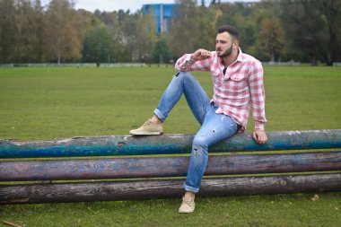 Genç yakışıklı Kovboy. Erkek çiftçi çiftliğindeki çitlerinde oturuyor. Kırsal alanlar, kırsal alanlar. Ağaçlar, tarlalar, çiftlik. Tasarım için stok fotoğrafları