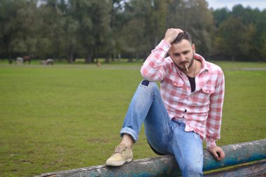 Genç yakışıklı Kovboy. Erkek çiftçi çiftliğindeki çitlerinde oturuyor. Kırsal alanlar, kırsal alanlar. Ağaçlar, tarlalar, çiftlik. Tasarım için stok fotoğrafları
