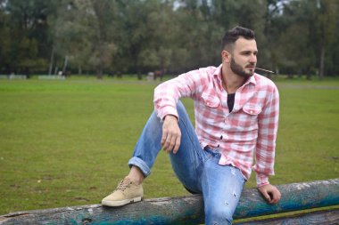 Genç yakışıklı Kovboy. Erkek çiftçi çiftliğindeki çitlerinde oturuyor. Kırsal alanlar, kırsal alanlar. Ağaçlar, tarlalar, çiftlik. Tasarım için stok fotoğrafları