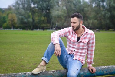 Genç yakışıklı Kovboy. Erkek çiftçi çiftliğindeki çitlerinde oturuyor. Kırsal alanlar, kırsal alanlar. Ağaçlar, tarlalar, çiftlik. Tasarım için stok fotoğrafları