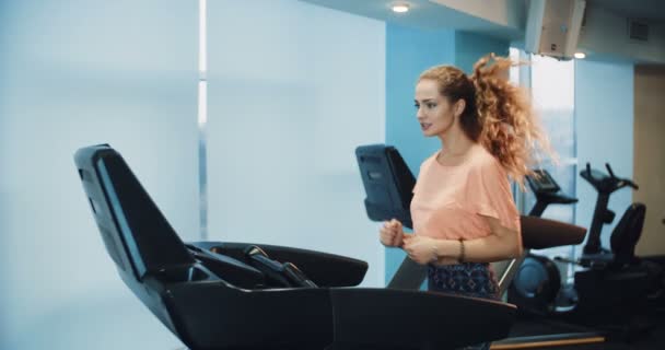 Attraktiva curly flicka kör på löpbandet i gymmet sport — Stockvideo