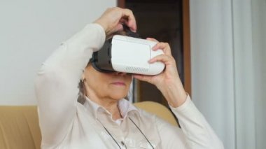 Orta üst düzey kadın görüntüsünü Vr gözlük oynarken kanepede oturuyor. İyi görünümlü kadın kıdemli Vr 360 gözlükle evde beyaz.