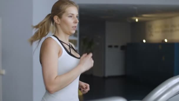 Vista lateral do treinamento de cardio de senhora em forma e em um ginásio. Mulher correndo em esteira . — Vídeo de Stock