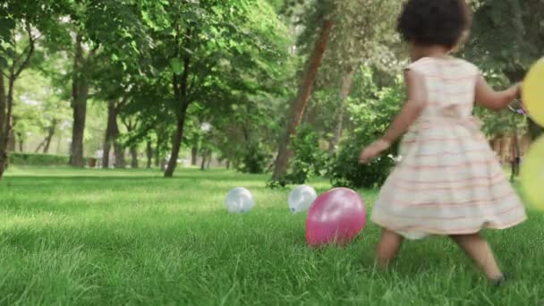Kleine afrikanisch-amerikanische Mädchen spielen mit bunten Luftballons im Park. — Stockvideo