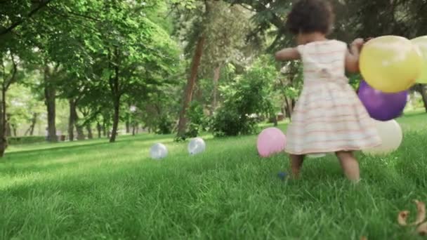 Маленькая африканско-американская девочка играет с разноцветными воздушными шарами в парке . — стоковое видео
