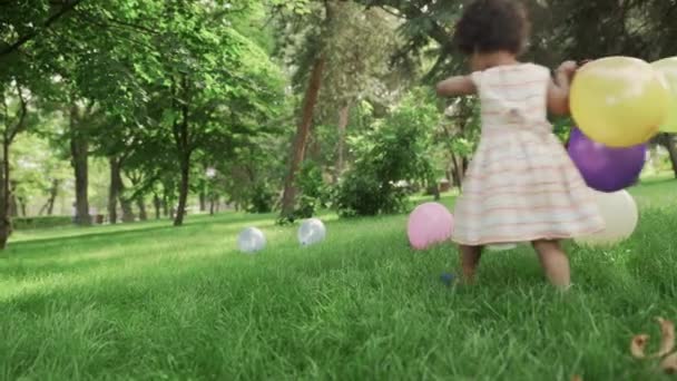 Little african-american girl play with multicolored balloons in the park. — Stock Video