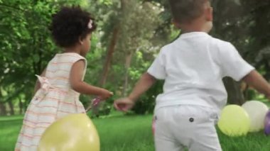 Küçük Afro-Amerikalı kız ve oğlan parkta renkli balonlarla oynuyorlar..