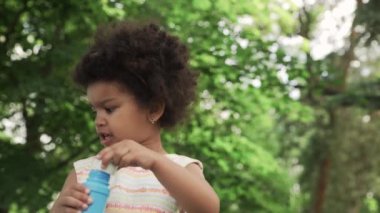 Küçük ve sevimli Afrikalı-Amerikalı kız parkta sabun köpüğü üflüyor..