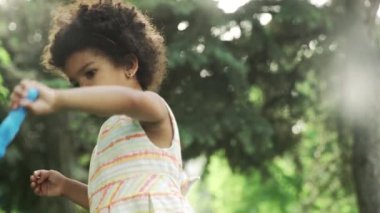 Küçük Afro-Amerikalı kız parkta sabun köpüğüyle oynuyor..