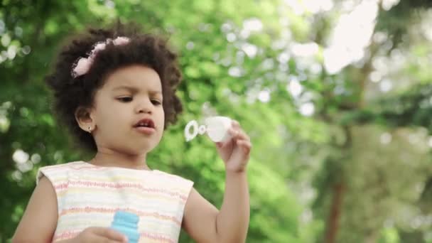 Primer plano de la chica afroamericana soplar burbujas de jabón en el parque . — Vídeos de Stock