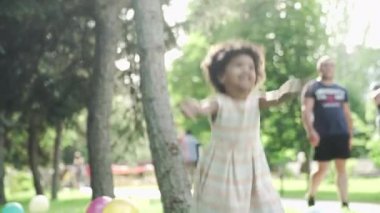 Küçük Afro-Amerikalı kız parkta oynar ve zıplar. Arka planda tanınmayan insanlar
