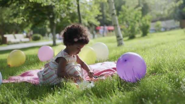 Little african-american girl is sitting in the park and drawing — Stock Video