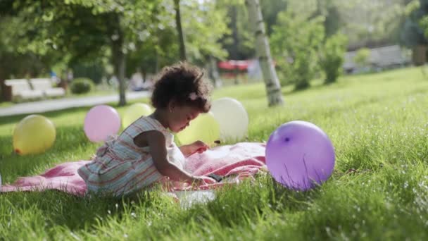 Little african-american girl is sitting in the park and drawing — Stock Video