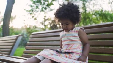 Afro-Amerikalı kız parkta tablette çizgi film izliyor.