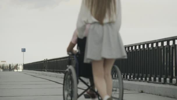 Gehandicapte man in rolstoel en zijn vriendin lopen op dijk — Stockvideo