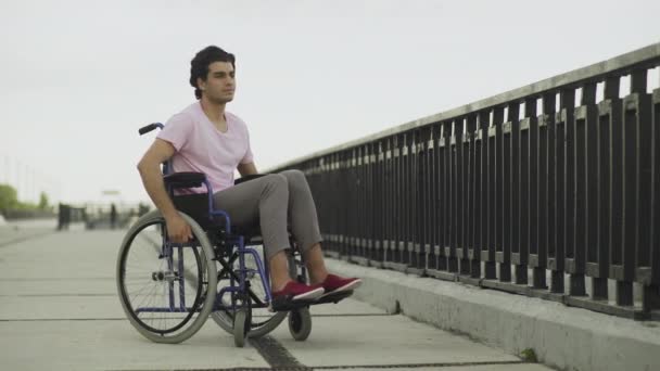 Печальный инвалид на инвалидной коляске прогулка в парке у реки и чувствовать себя одиноким — стоковое видео