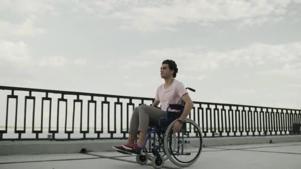 Несчастный человек едет на инвалидной коляске вдоль набережной — стоковое видео