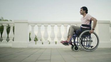 Tekerlekli sandalyedeki genç adam halka açık bir bahçede yol boyunca gidiyor..