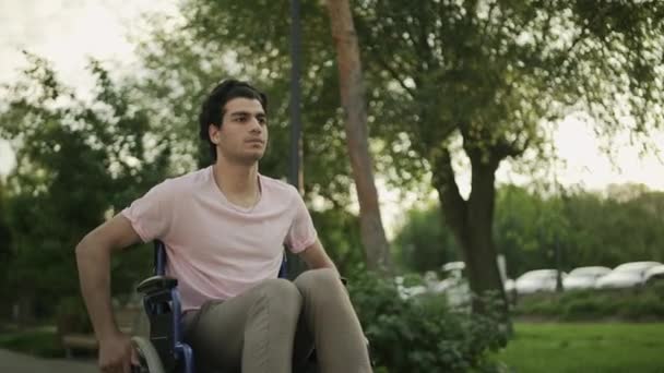 Behinderter junger Mann im Rollstuhl fährt in Park. — Stockvideo