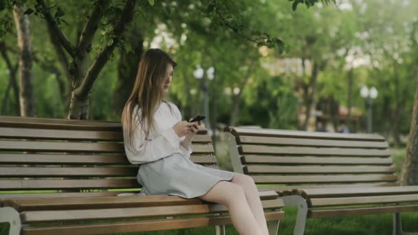 Un hombre joven en silla de ruedas monta en el parque y una mujer joven se sienta en el banco y lo mira tristemente — Vídeos de Stock