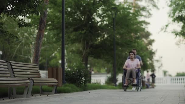 Gelukkige gehandicapte man in een rolstoel met gelukkige jongeman op het stadspark — Stockvideo