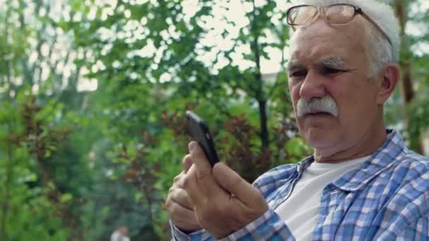 Un anciano con bigote intenta usar su teléfono móvil, pero no puede entender cómo — Vídeo de stock