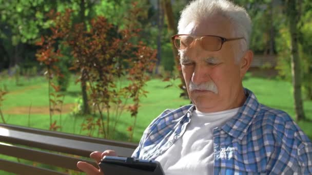 Un homme âgé avec des lunettes lit un moment tendu dans un livre — Video